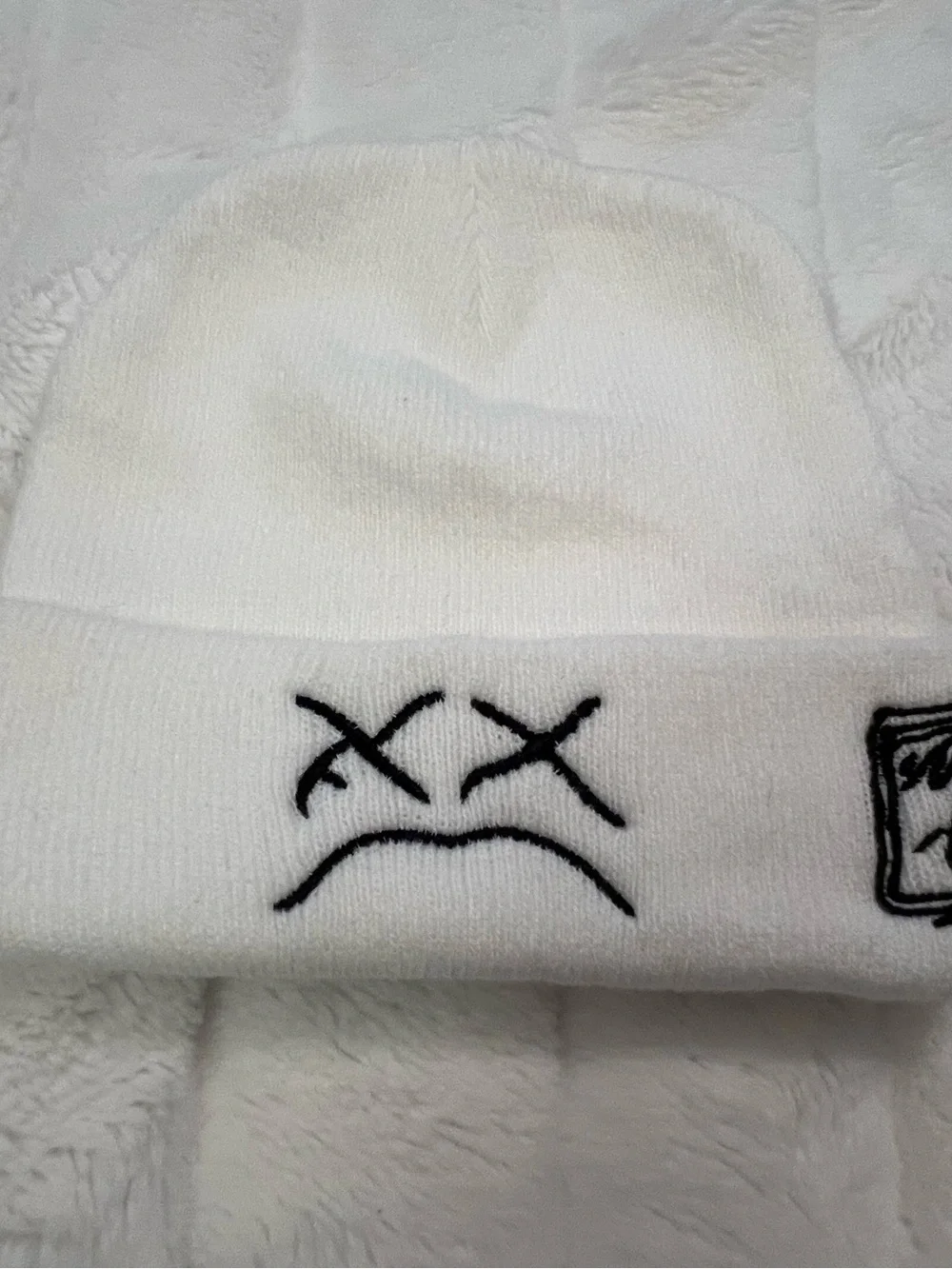 White KAWS beanie with black embroidered sad face and box logo